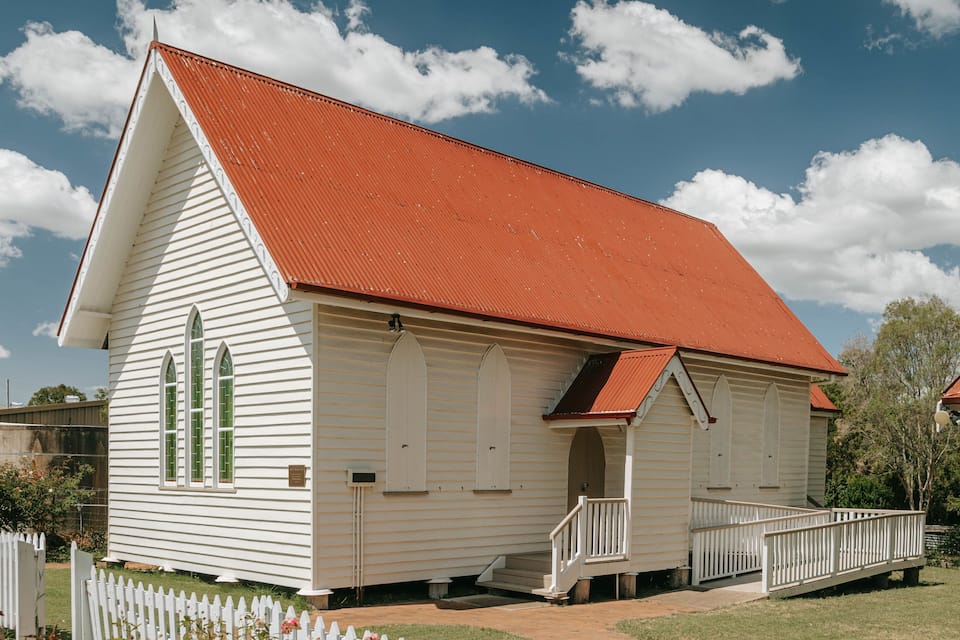 Une église en bois peinte en blanc, avec un toit rouge et une petite clôture blanche devant.