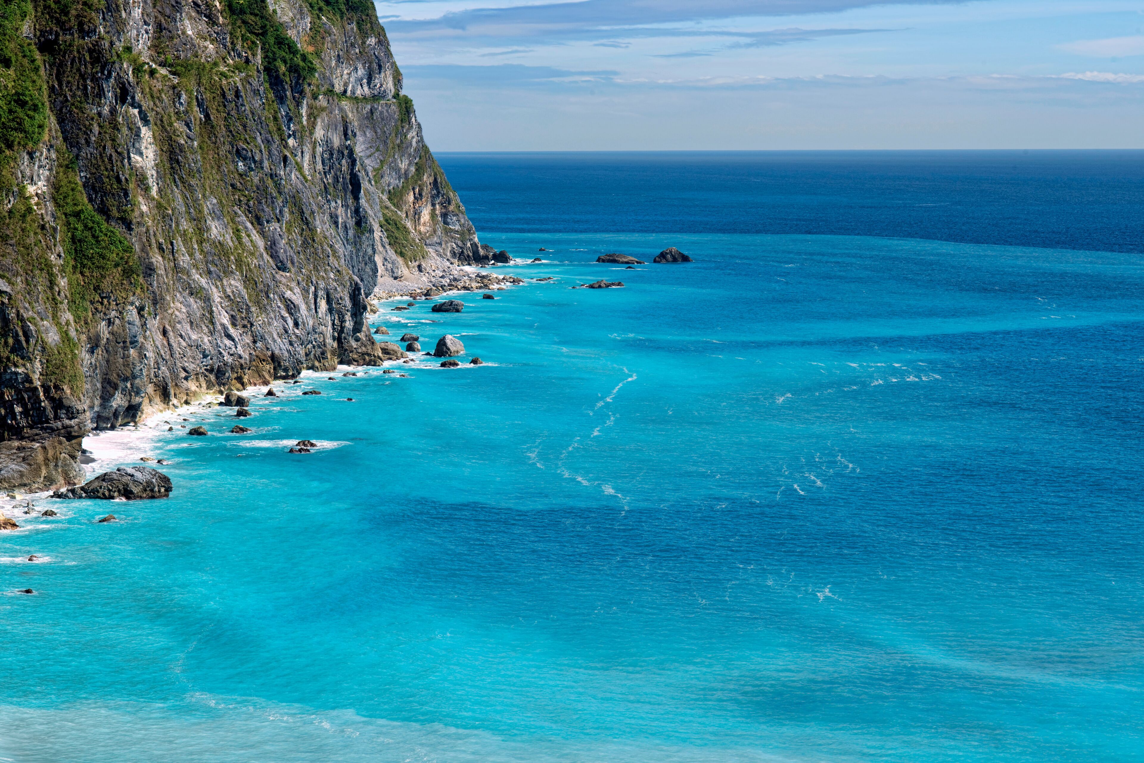 A coastal cliff with turquoise waters and scattered rocks.
