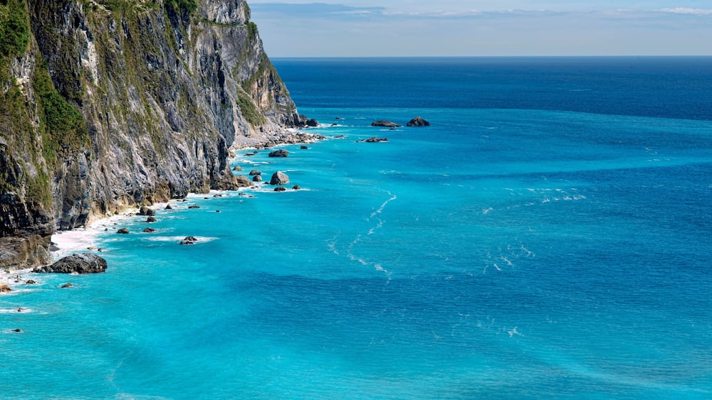 A coastal cliff with turquoise waters and scattered rocks.