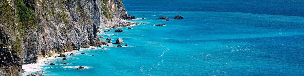 A coastal cliff with turquoise waters and scattered rocks.