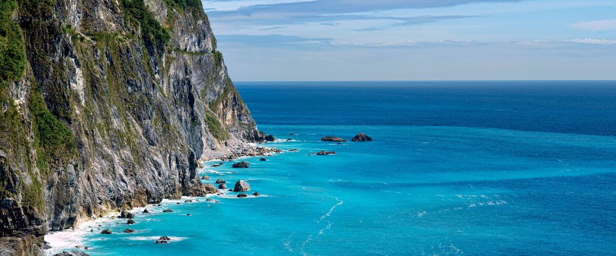 A coastal cliff with turquoise waters and scattered rocks.