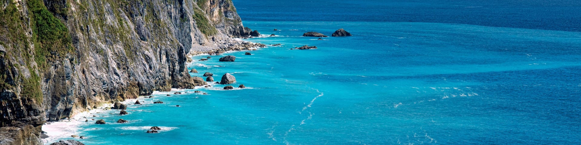 A coastal cliff with turquoise waters and scattered rocks.