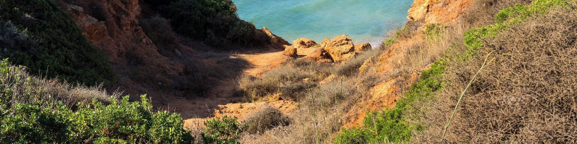 A coastal landscape with cliffs, clear blue sea, and a lighthouse in the distance.