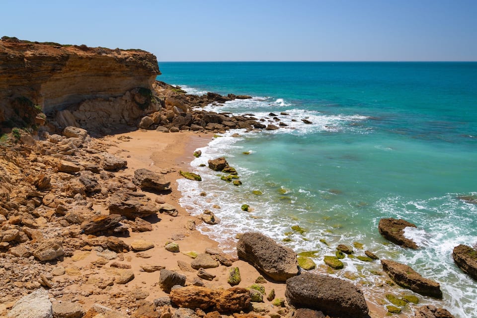 A rocky beach with a cliff and ocean waves.