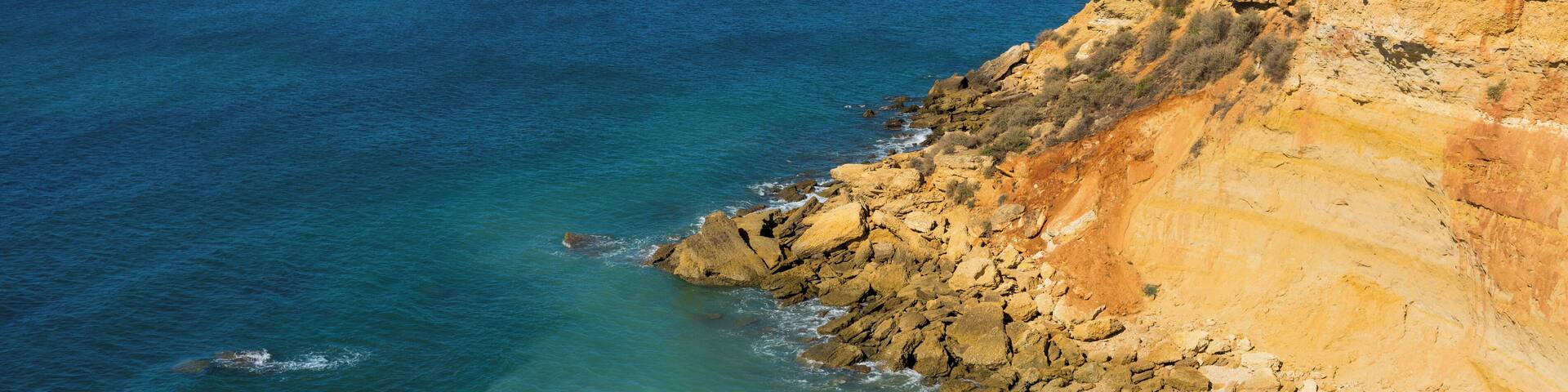 Un paisaje costero con un litoral rocoso, aguas azules cristalinas y un faro distante.