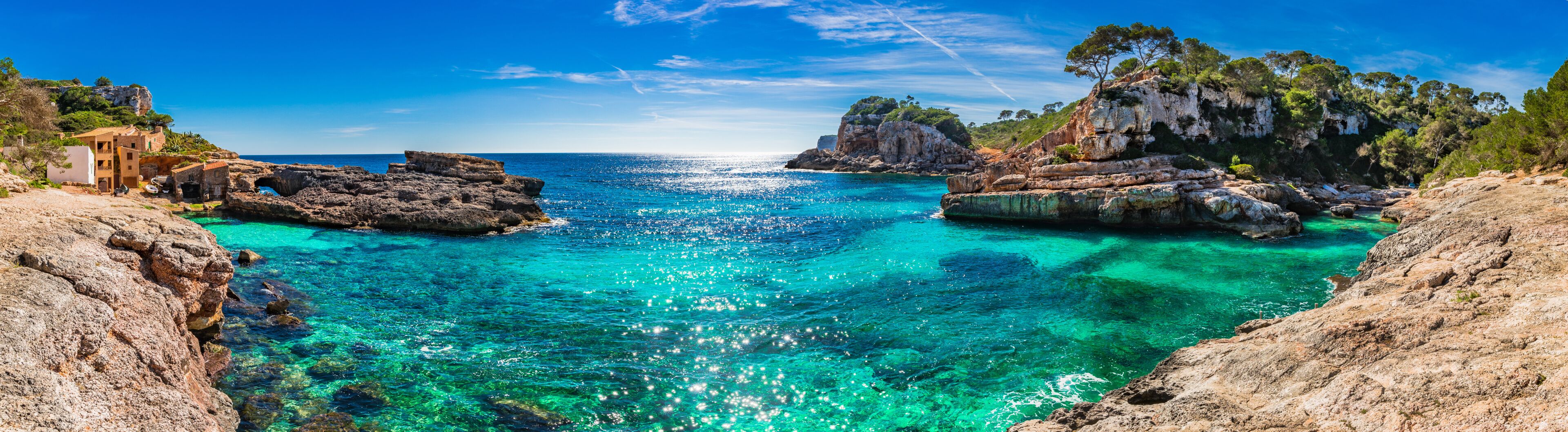 A coastal landscape with clear turquoise waters, rocky formations, and a cliff with vegetation.