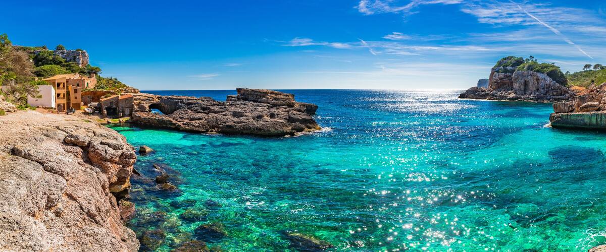 A coastal landscape with clear turquoise waters, rocky formations, and a cliff with vegetation.