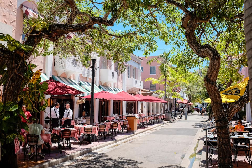 Rua com cafés ao ar livre, guarda-sóis vermelhos e mesas com cadeiras.