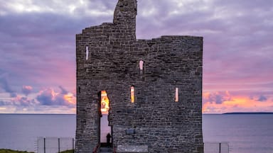 A stone tower with a fire burning inside, set against a sunset over water.