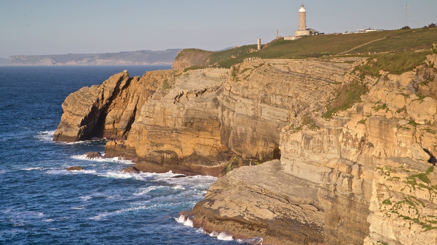 A coastal cliff with a lighthouse and rocky waves crashing against it.