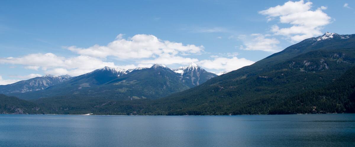 A lake surrounded by mountains with snow-capped peaks and dense forests.