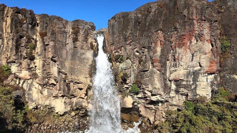 A waterfall cascading down a rocky cliff into a pool surrounded by dense vegetation.