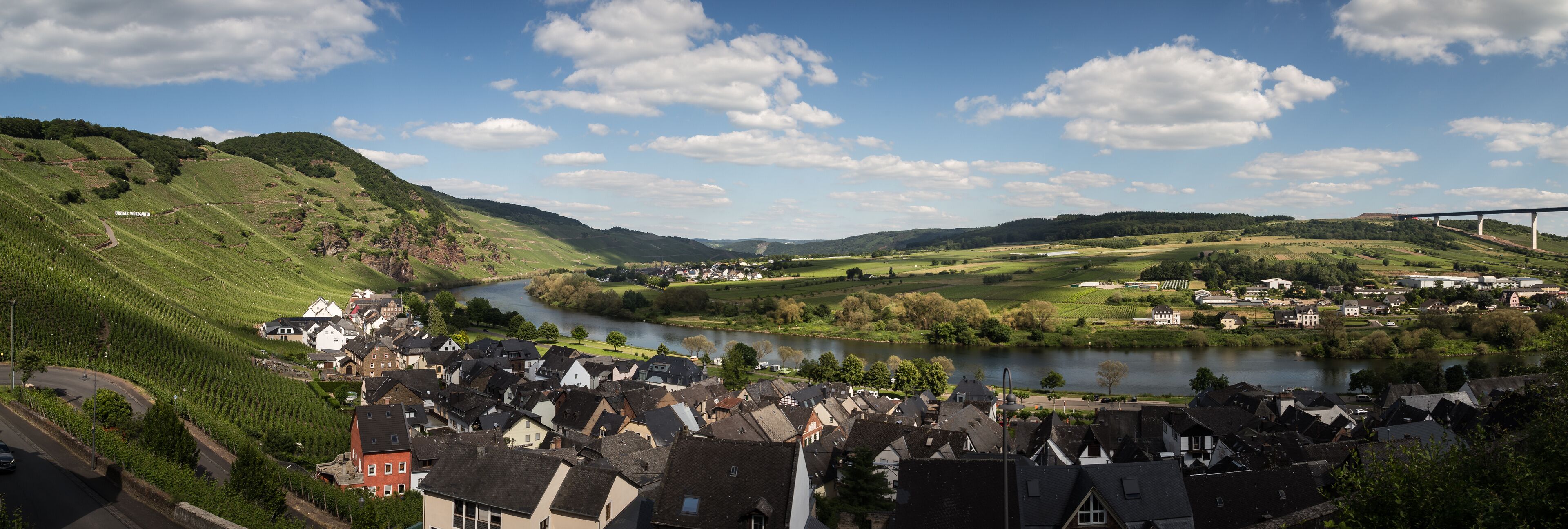 A river flowing through a valley with a bridge in the distance, surrounded by green hills and a small town with traditional houses.