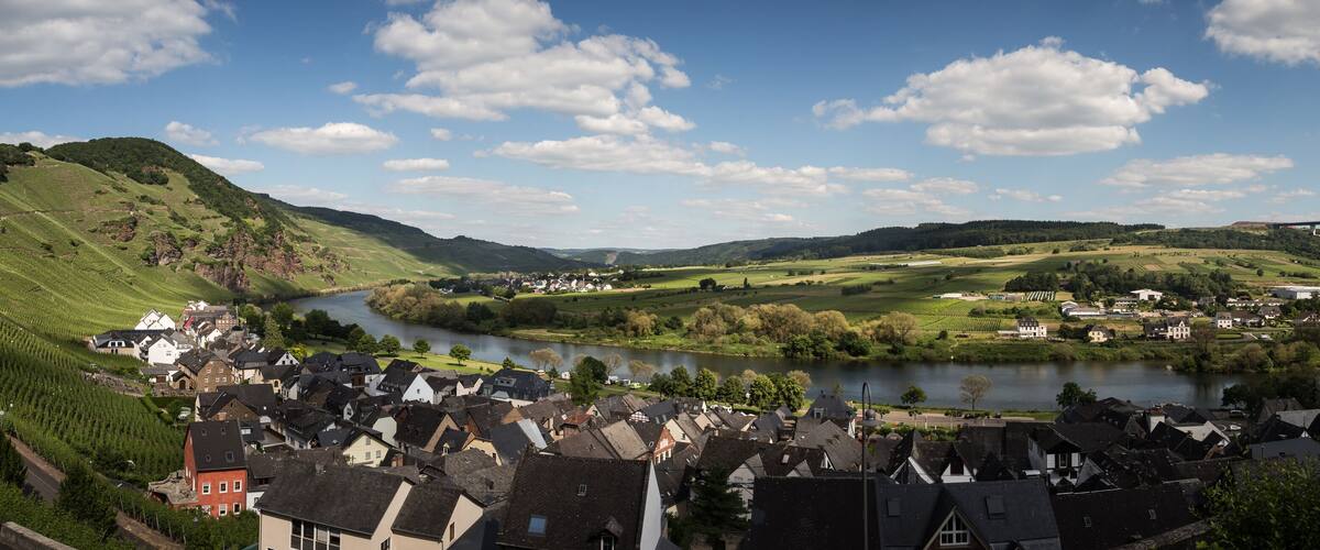 A river flowing through a valley with a bridge in the distance, surrounded by green hills and a small town with traditional houses.