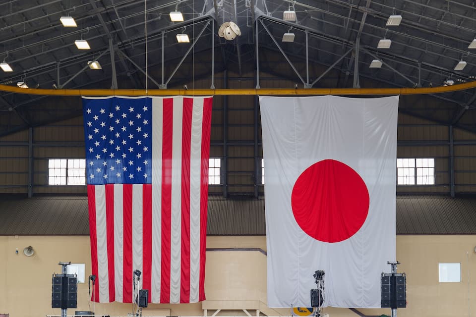 Two large flags, an American flag and a Japanese flag, hanging in a large industrial building.