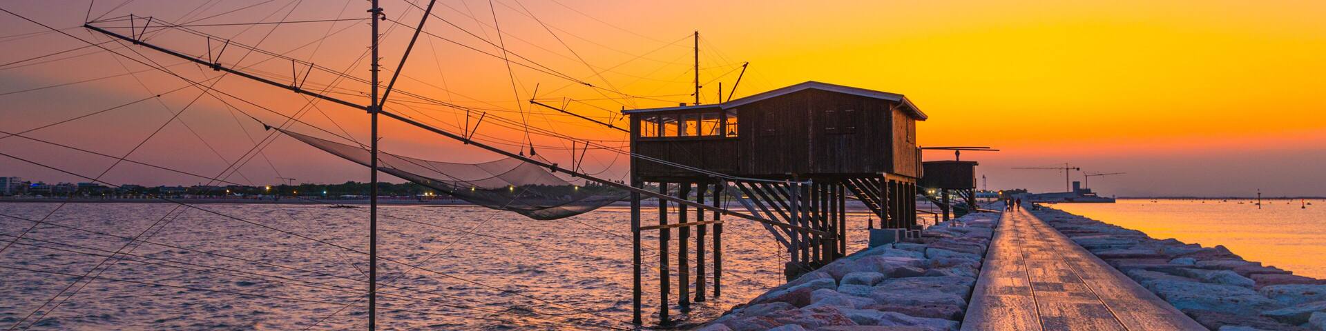 A pier extending into a body of water at sunset with fishing nets and a wooden structure.