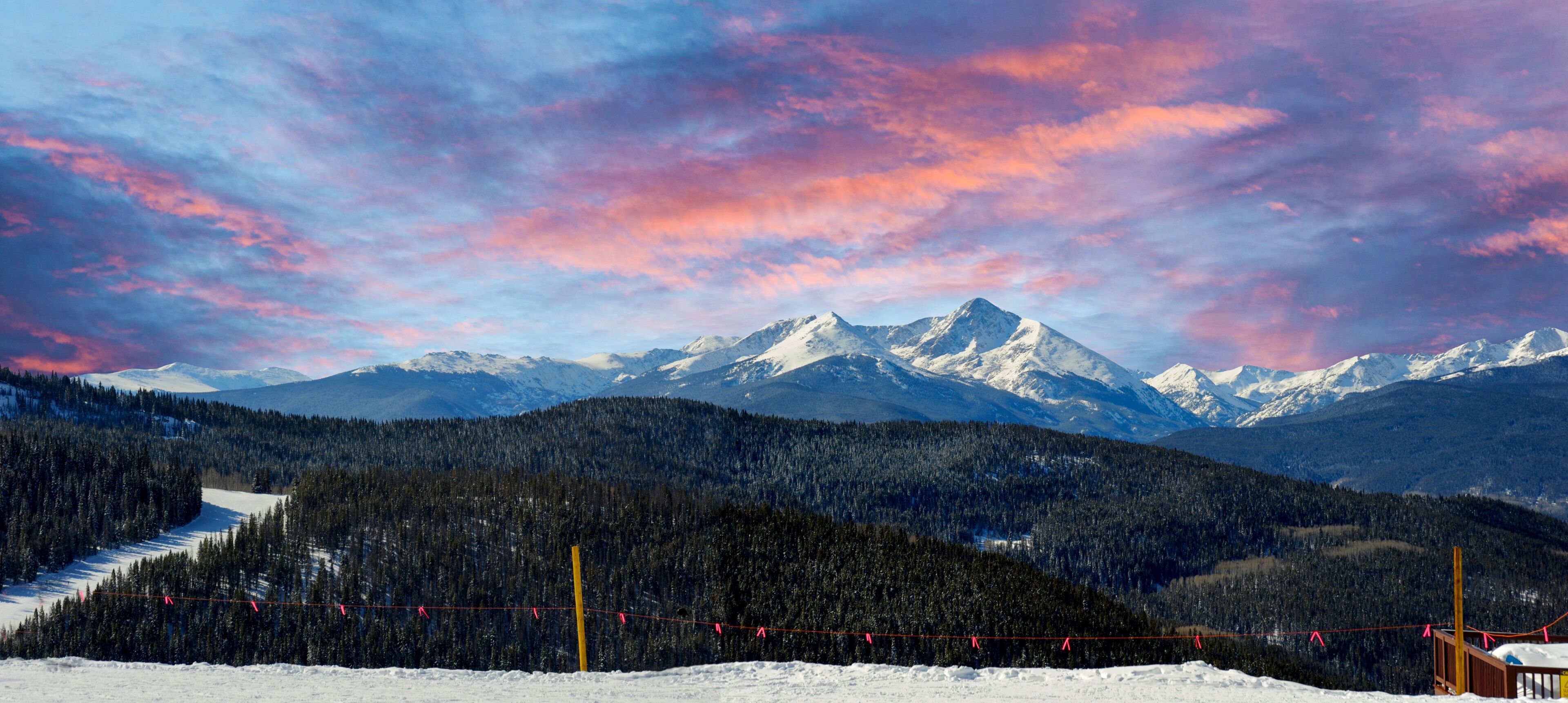 A snow-covered mountain range with a forested valley and a ski lift.