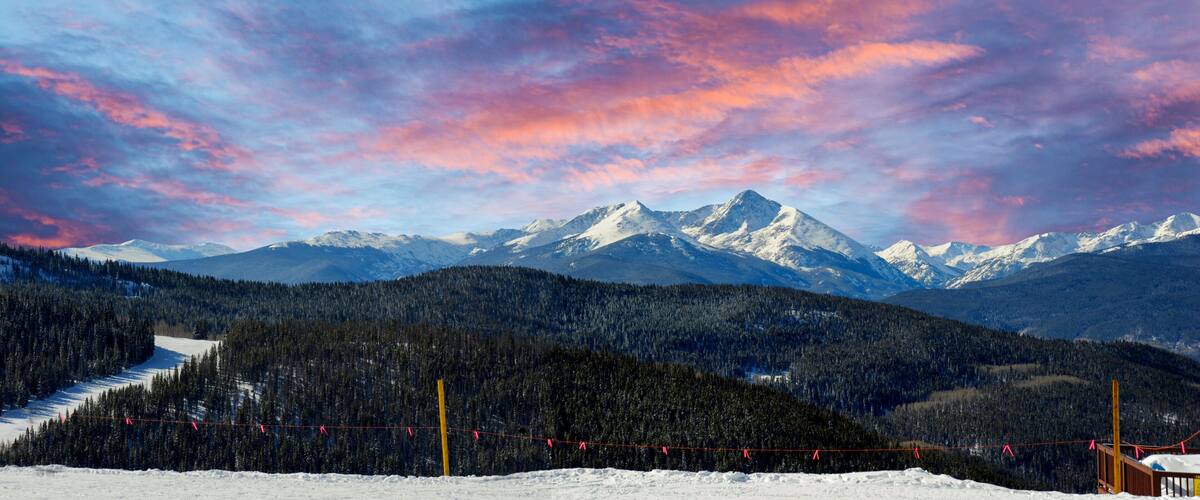 A snow-covered mountain range with a forested valley and a ski lift.