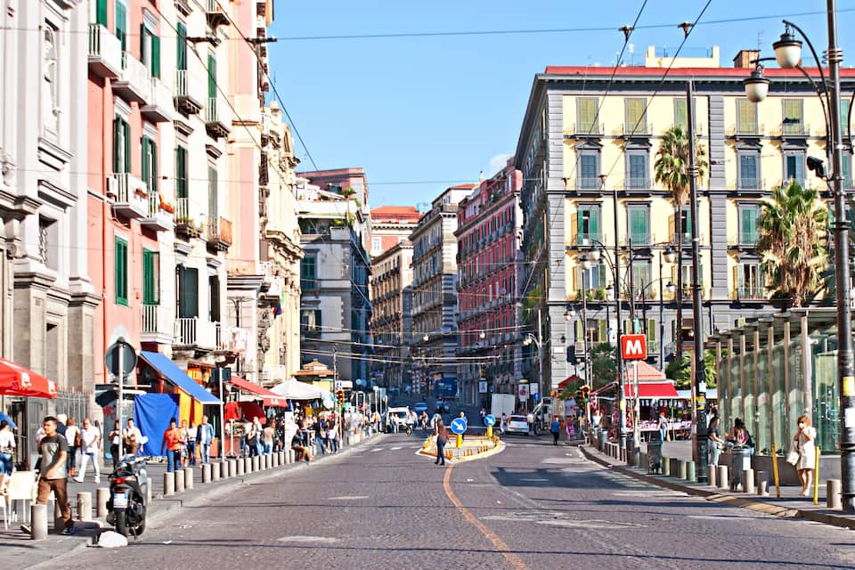 Une rue animée en plein cœur de la ville, bordée d’immeubles aux couleurs vives, avec une ligne de tramway et des piétons.