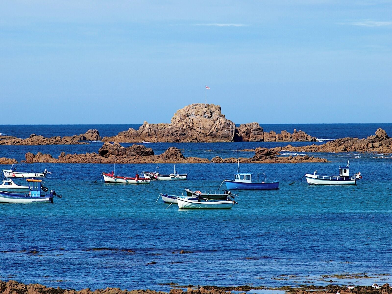 A rocky coastline with several small boats anchored in calm waters.