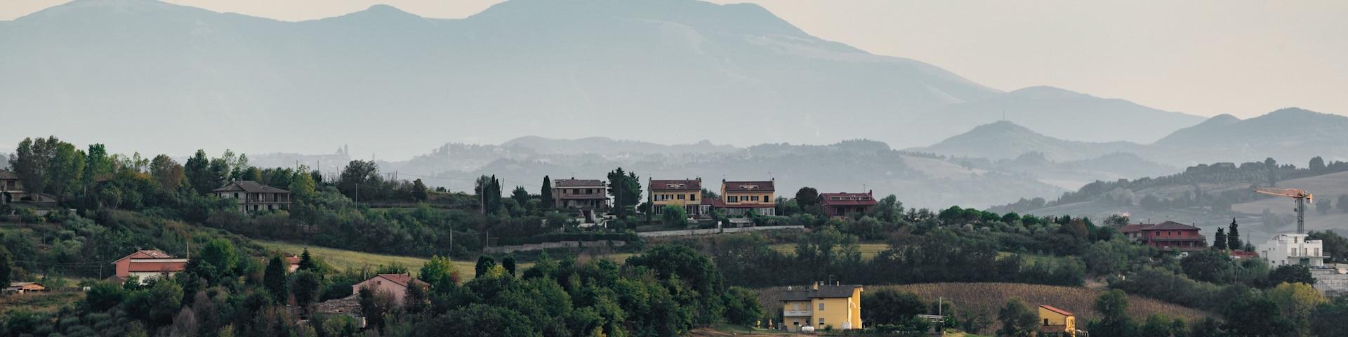 A rural landscape with rolling hills, scattered houses, and a distant mountain range.