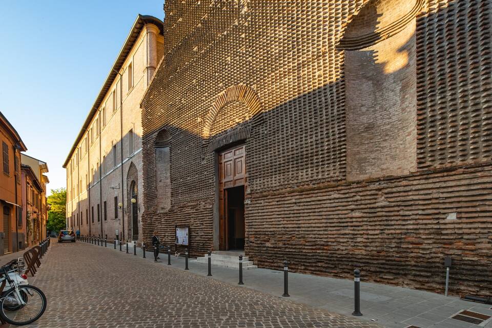 Calle adoquinada bordeada de edificios históricos, incluyendo un muro de ladrillo con un diseño en espiral y una puerta de madera tradicional.