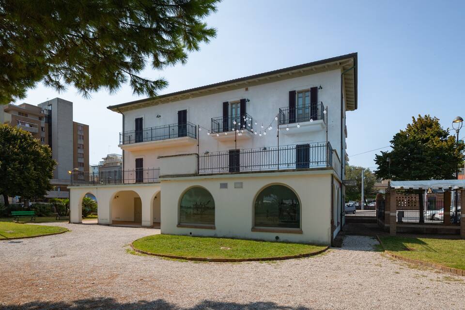 A two-story building with a balcony, surrounded by a gravel courtyard and trees.