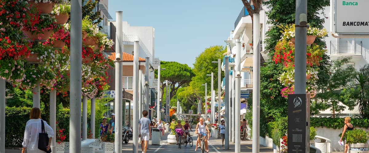A pedestrian street lined with white buildings, potted plants, and people walking and cycling.