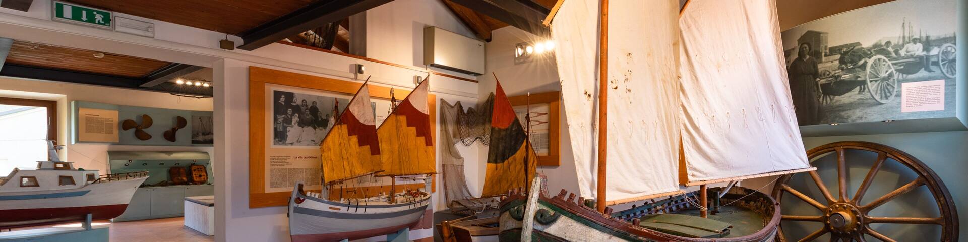A museum exhibit with historical sailing ships and a large wooden wheel.
