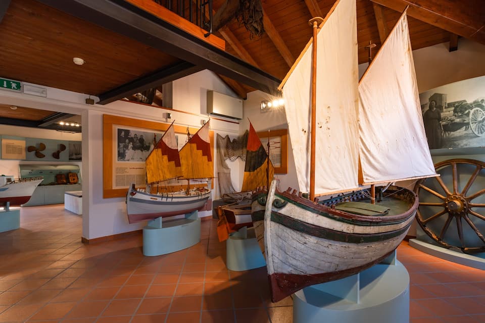 Uma exposição de museu com navios a vela históricos e uma grande roda de madeira.