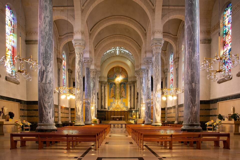 A church interior with marble columns, stained glass windows, and wooden pews.