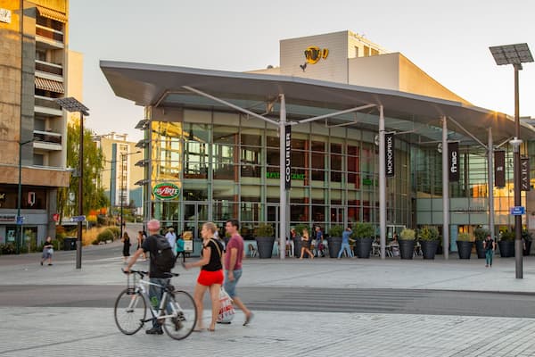 A modern building with a glass facade and a large overhang, surrounded by pedestrians and cyclists.