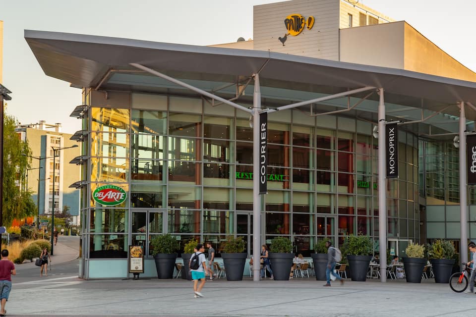 A modern building with a glass facade, outdoor seating, and a sign for 'Del Arte Restaurant'.