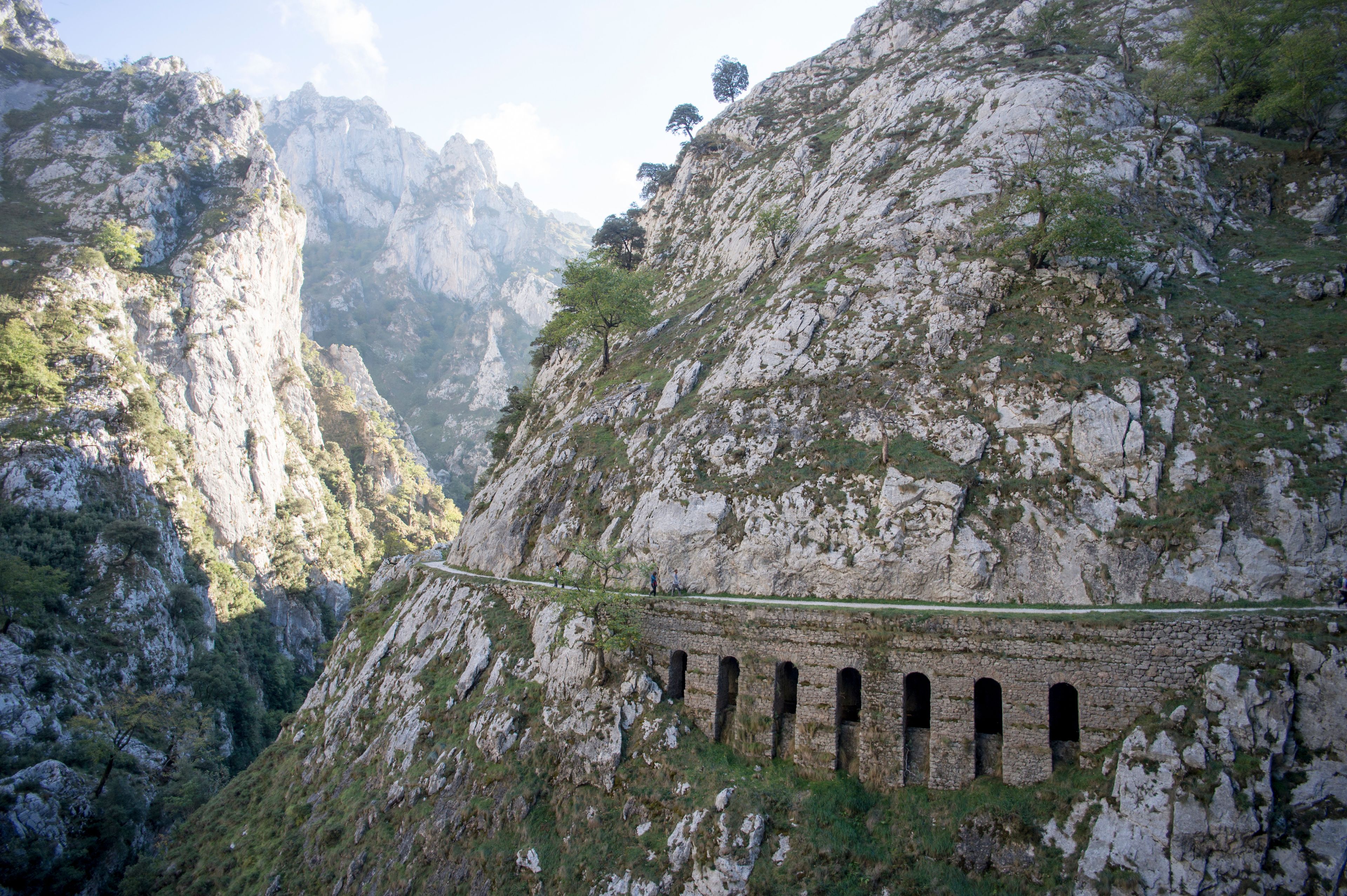 Un paisaje montañoso con un camino estrecho que atraviesa una garganta rocosa, bordeada por acantilados empinados y vegetación escasa.