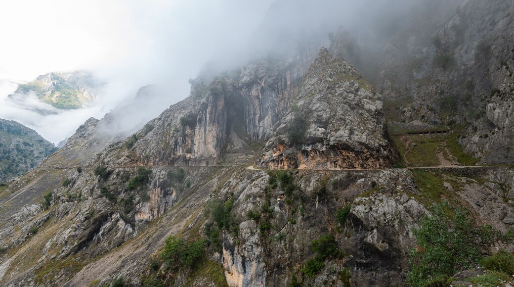 Un paisaje montañoso y accidentado con riscos escarpados y un sendero sinuoso que serpentea por el terreno rocoso.