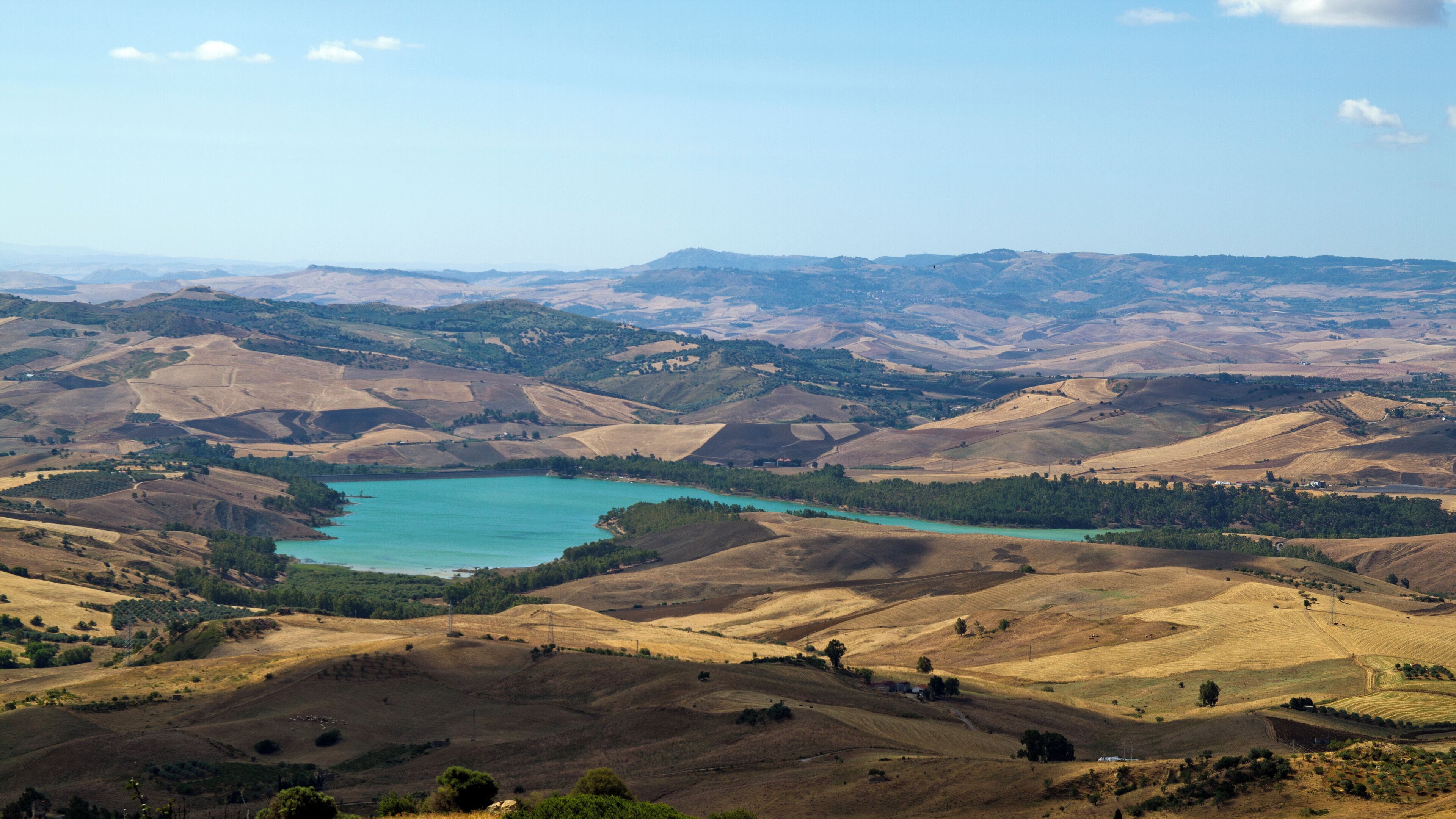 A panoramic view of rolling hills and a turquoise lake surrounded by greenery.