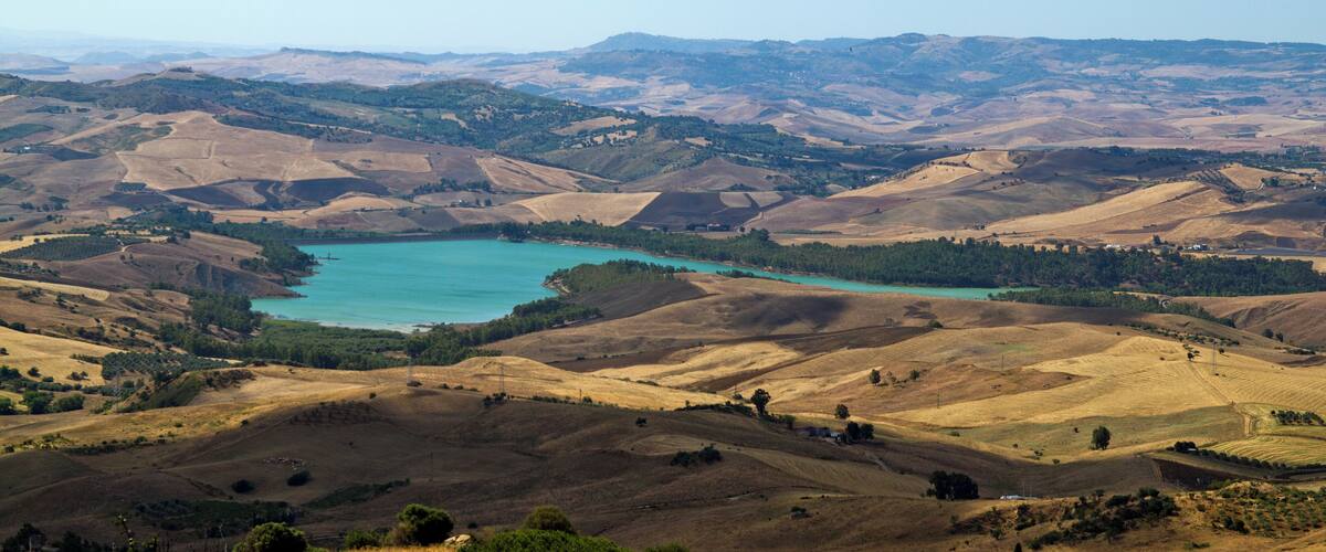 A panoramic view of rolling hills and a turquoise lake surrounded by greenery.