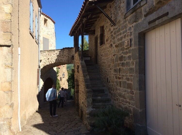 A narrow stone alleyway with a stone archway, a staircase, and a building with a wooden door.