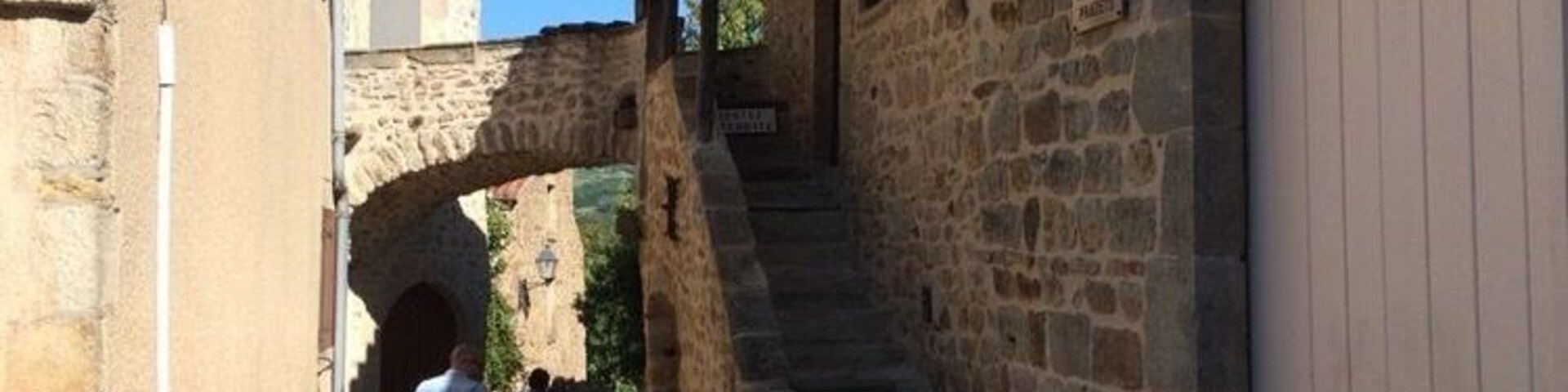 A narrow stone alleyway with a stone archway, a staircase, and a building with a wooden door.