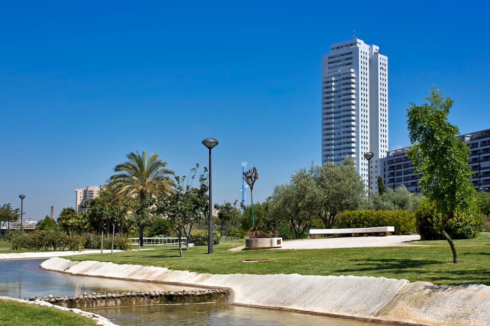 A park with a pond, palm trees, a statue, and a tall building in the background.