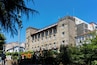A historic building with a castle-like facade, surrounded by lush greenery and modern structures.