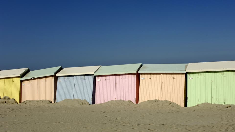 A row of colorful beach huts with a clear blue sky in the background.