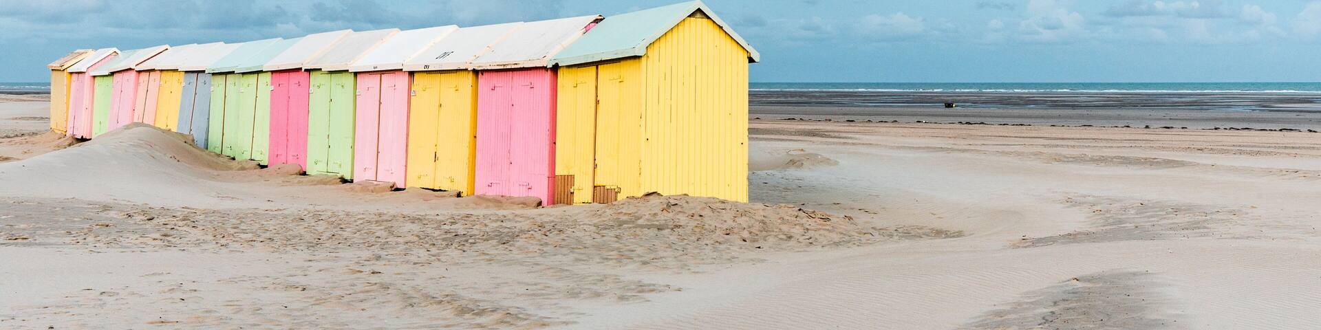A row of colorful beach huts along a sandy beach with a cloudy sky.