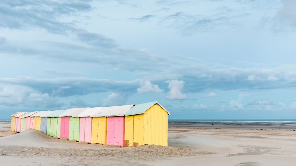 A row of colorful beach huts along a sandy beach with a cloudy sky.