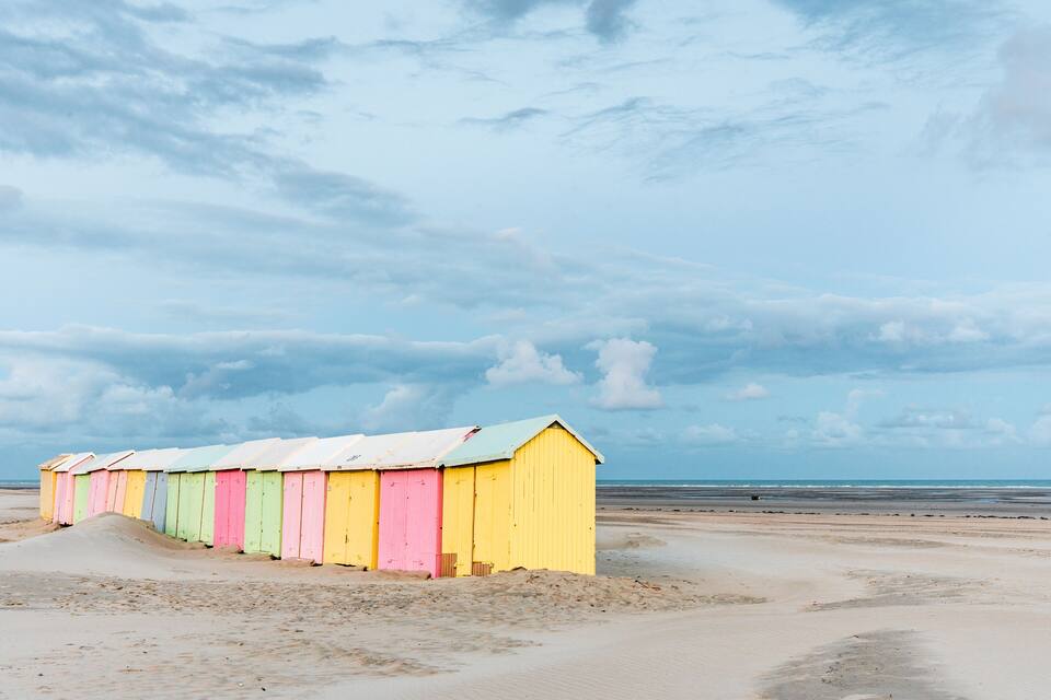 A row of colorful beach huts along a sandy beach with a cloudy sky.