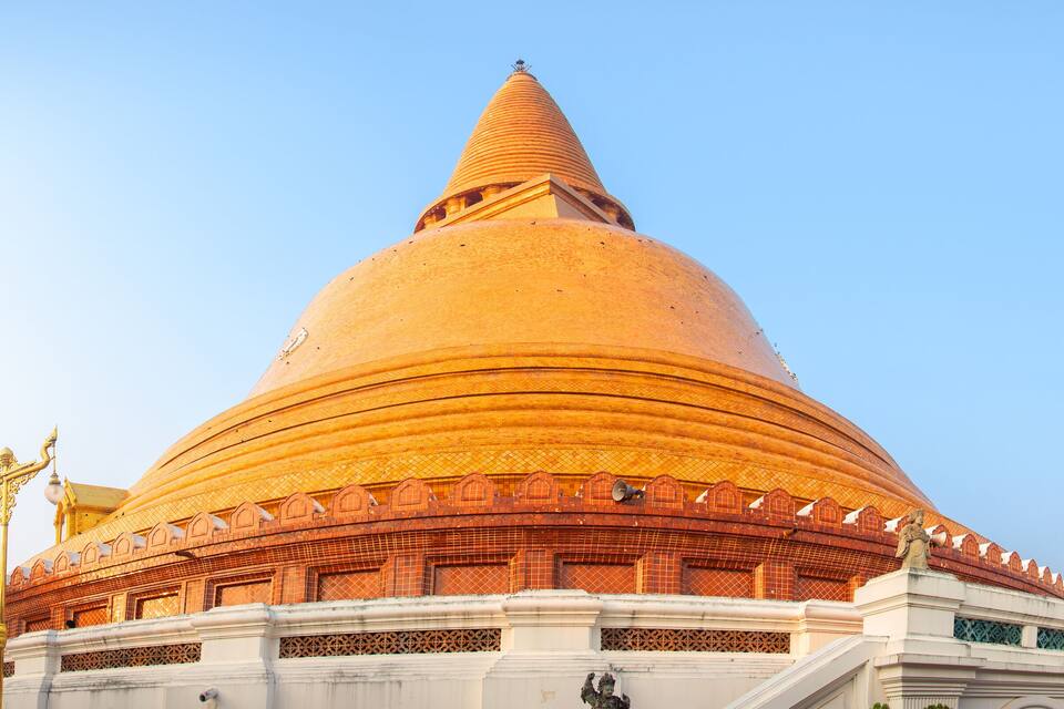 A golden stupa with a pointed spire, surrounded by white walls and golden statues.