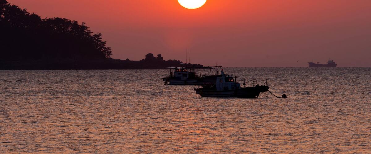 A sunset over a calm sea with two boats.
