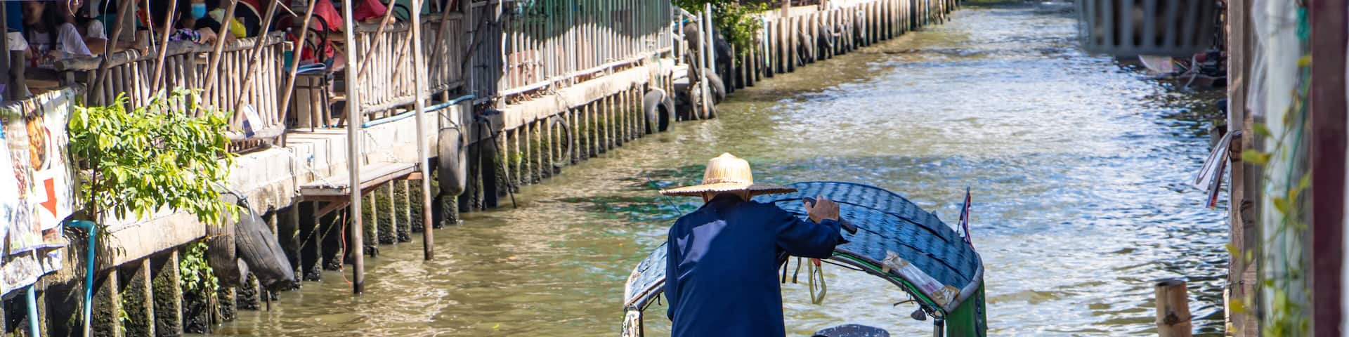 A man drive a gondola boat with tourist in a water canal at the Khlong Lat Mayom Floating Market, Thailand.