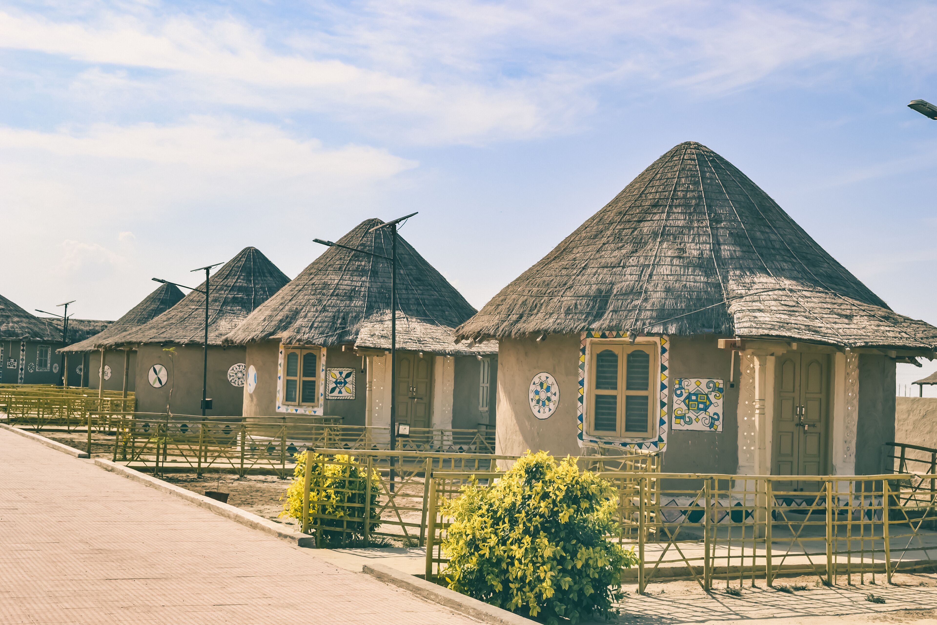 A row of thatched-roof huts with a gate and yellow railings in the foreground.
