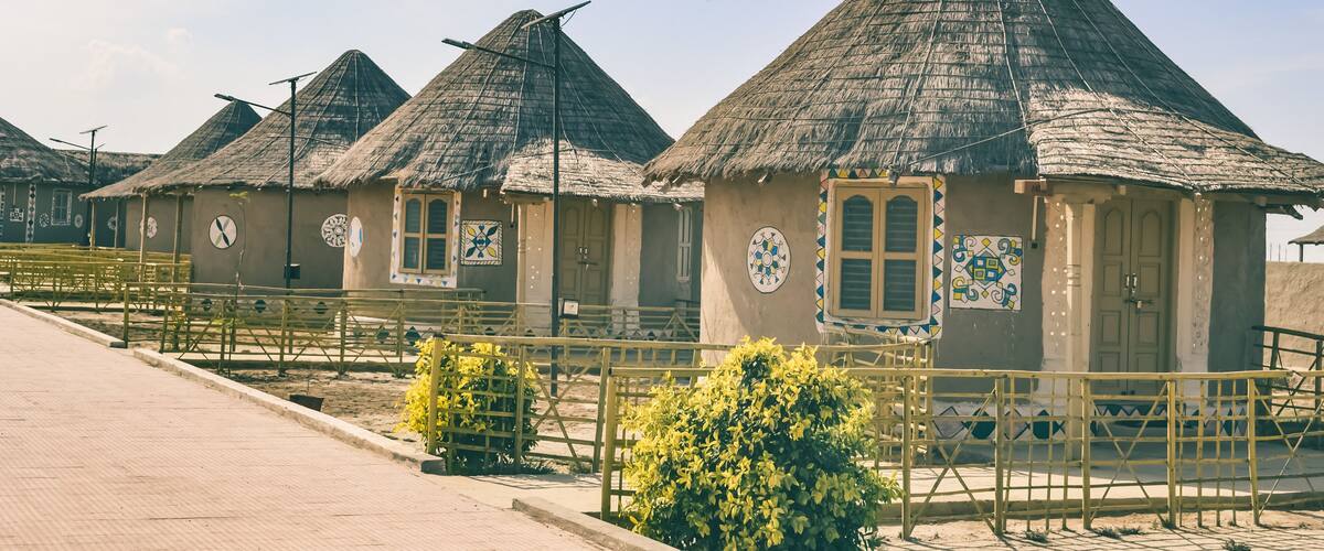 A row of thatched-roof huts with a gate and yellow railings in the foreground.